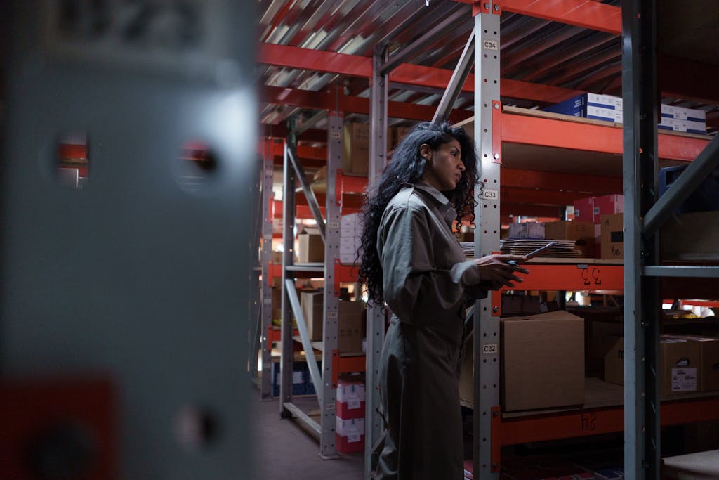 An adult woman in uniform checking inventory in a warehouse aisle.