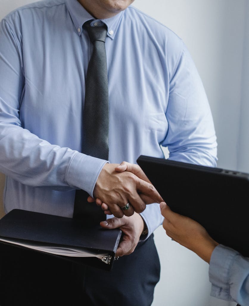 Business handshake between colleagues in a formal office meeting setting.